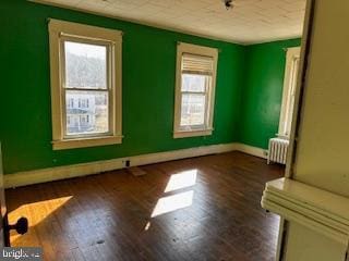 unfurnished room with radiator heating unit, plenty of natural light, and wood finished floors