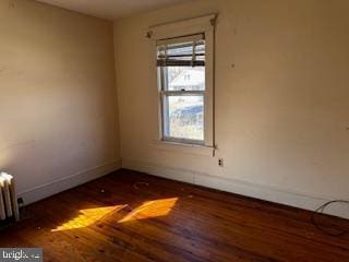 spare room with baseboards, wood finished floors, and radiator