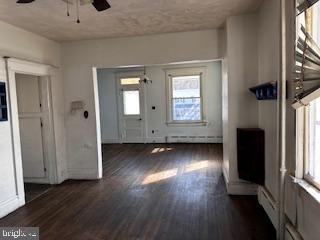 unfurnished living room featuring a baseboard heating unit, a ceiling fan, and wood finished floors