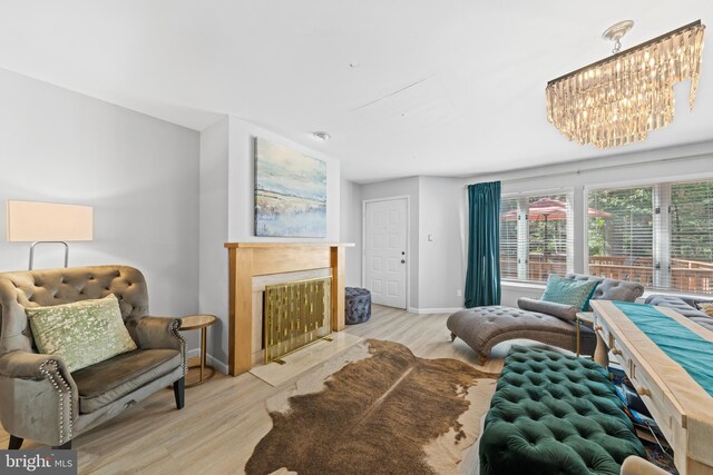 living area featuring light wood-type flooring, baseboards, a notable chandelier, and a fireplace