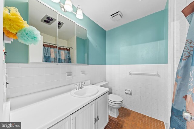 bathroom with vanity, a wainscoted wall, visible vents, tile walls, and toilet