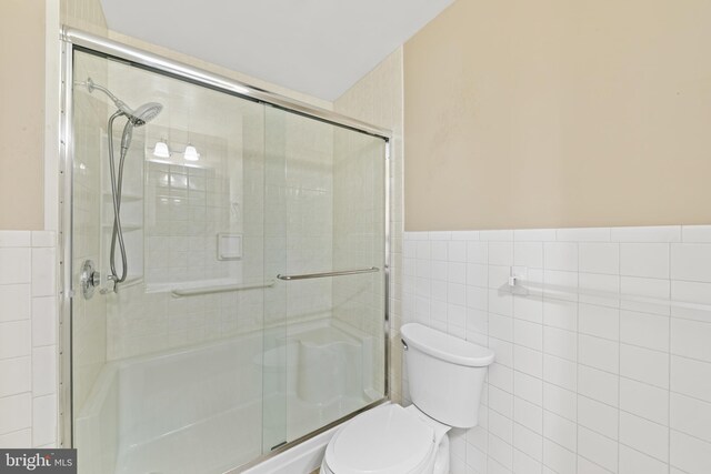 full bathroom featuring wainscoting, a stall shower, toilet, and tile walls