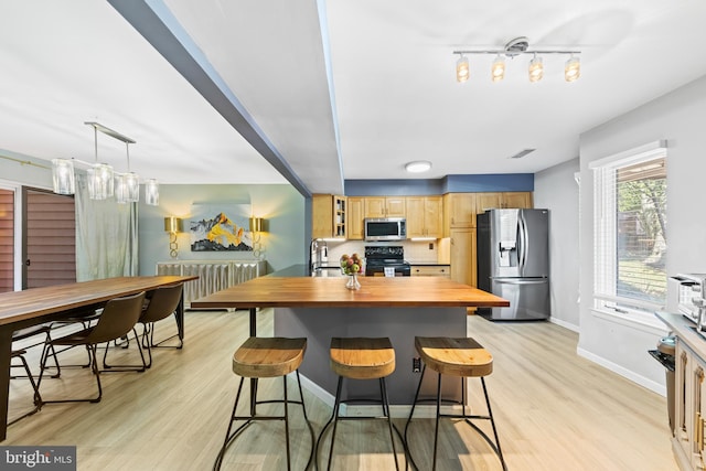 kitchen featuring wooden counters, a breakfast bar, a sink, stainless steel appliances, and light wood-type flooring