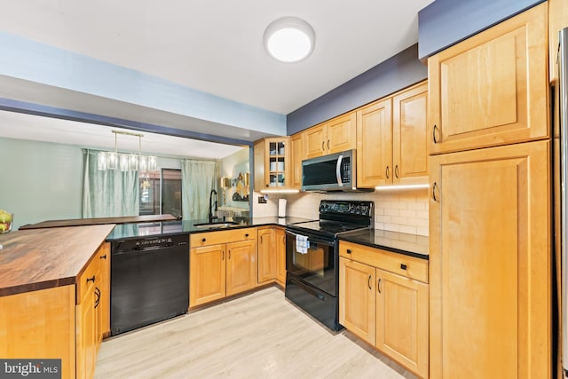 kitchen featuring light brown cabinets, a peninsula, a sink, black appliances, and glass insert cabinets