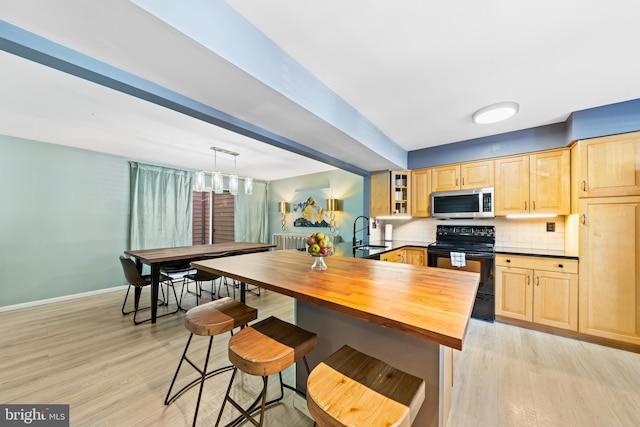 kitchen featuring stainless steel microwave, black range with electric cooktop, light brown cabinets, and tasteful backsplash