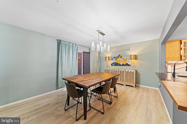 dining space with baseboards, an inviting chandelier, and light wood-style flooring