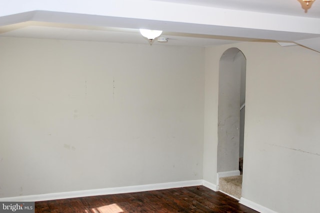 empty room with arched walkways, dark wood-style floors, and baseboards