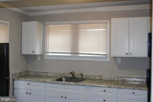 kitchen with a sink, white cabinetry, freestanding refrigerator, light stone countertops, and crown molding