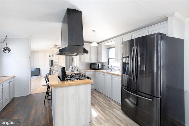 kitchen featuring ventilation hood, light wood-type flooring, butcher block counters, and black appliances