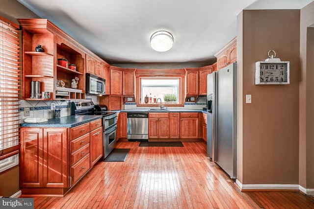 kitchen featuring open shelves, light wood-style flooring, appliances with stainless steel finishes, a sink, and baseboards