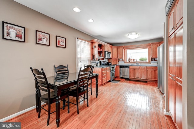 kitchen featuring light wood finished floors, baseboards, stainless steel appliances, open shelves, and a sink