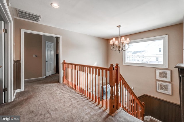 corridor featuring carpet, visible vents, a notable chandelier, and an upstairs landing