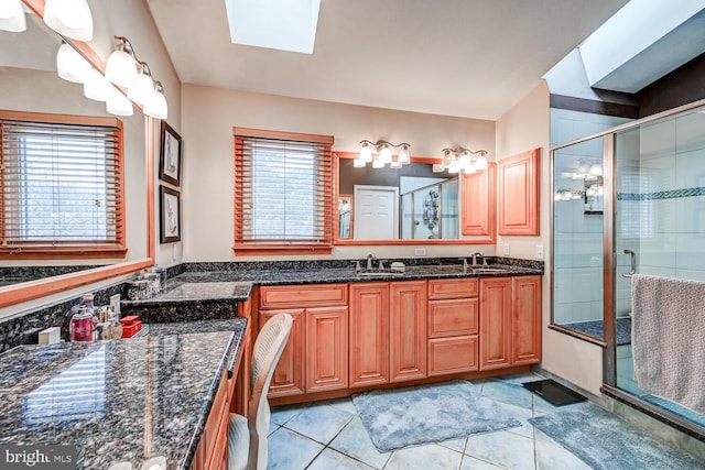 full bathroom featuring double vanity, a skylight, tile patterned floors, a shower stall, and a sink