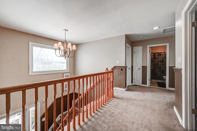 corridor featuring visible vents, wainscoting, carpet flooring, an upstairs landing, and a chandelier