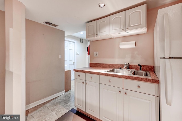 kitchen featuring light tile patterned floors, visible vents, white cabinets, freestanding refrigerator, and a sink