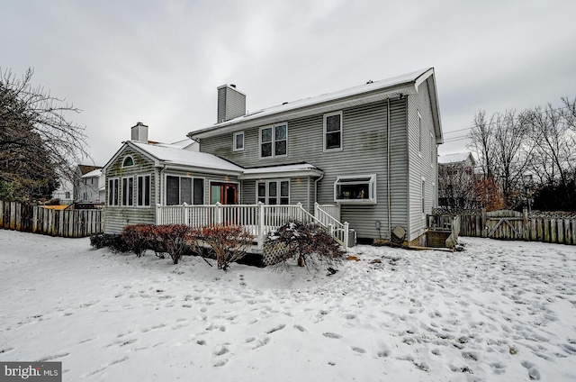 snow covered back of property with a deck, a sunroom, fence, and a chimney