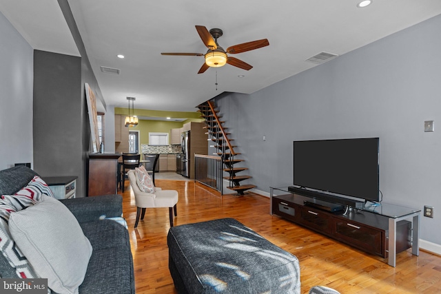 living area with recessed lighting, visible vents, light wood-style flooring, stairway, and baseboards