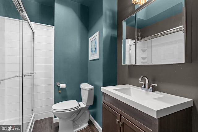 bathroom with a tile shower, wood finished floors, toilet, and baseboards