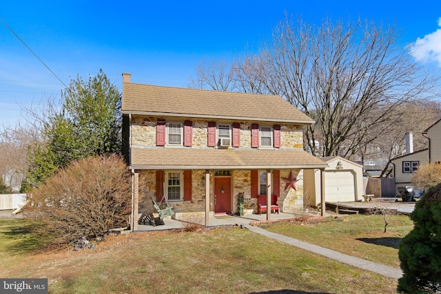 view of front of property with covered porch, a front yard, a garage, stone siding, and an outdoor structure