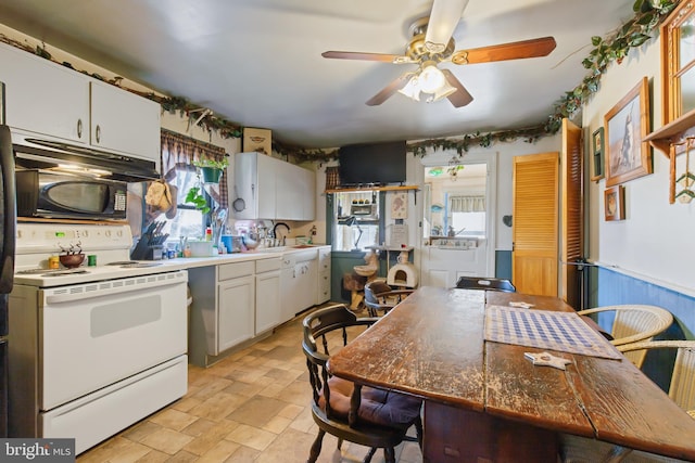 kitchen with a sink, white cabinets, wainscoting, stone finish floor, and white electric range oven