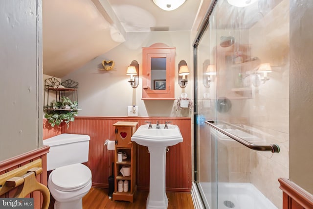 bathroom featuring toilet, a stall shower, wood finished floors, and wainscoting