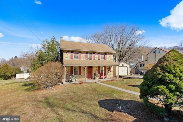 view of front of home with a garage, stone siding, an outbuilding, covered porch, and a front lawn