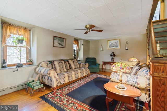 living room featuring stairs, ceiling fan, baseboard heating, and wood finished floors