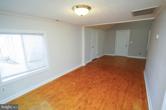 unfurnished room featuring visible vents, baseboards, vaulted ceiling, ornamental molding, and light wood-type flooring