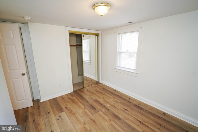 unfurnished bedroom with a closet, wood finished floors, visible vents, and baseboards