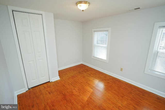 unfurnished bedroom featuring hardwood / wood-style flooring, baseboards, visible vents, and a closet