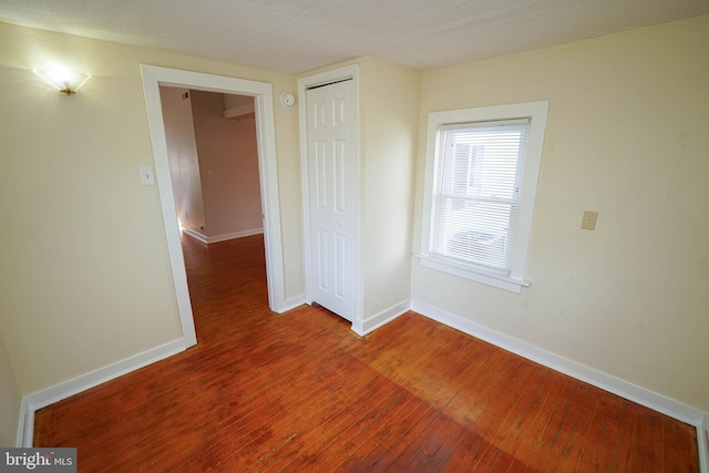 empty room featuring a textured ceiling, wood-type flooring, and baseboards