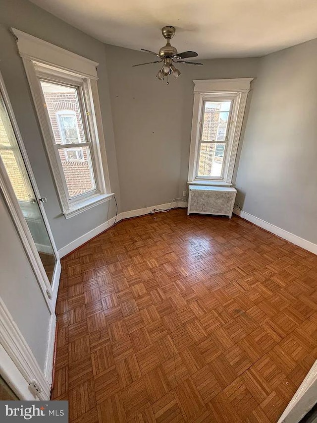 unfurnished room with baseboards, a ceiling fan, and radiator