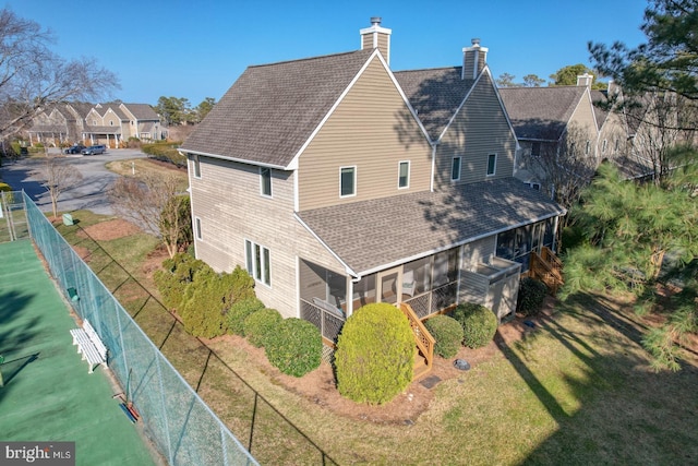 exterior space featuring a yard, fence, a sunroom, and roof with shingles