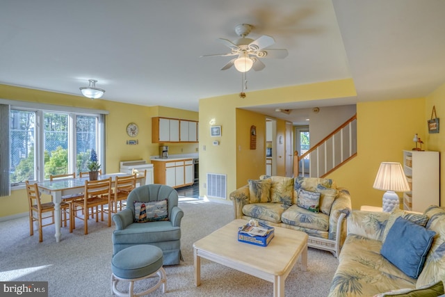 living room with visible vents, light carpet, a ceiling fan, stairway, and baseboards