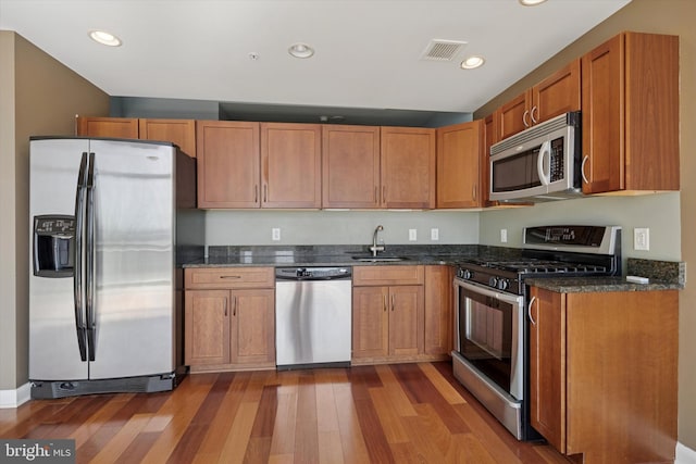 kitchen with stainless steel appliances, a sink, visible vents, dark stone counters, and dark wood finished floors