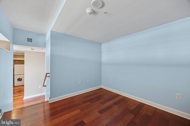 empty room featuring baseboards, wood finished floors, and stacked washer / drying machine