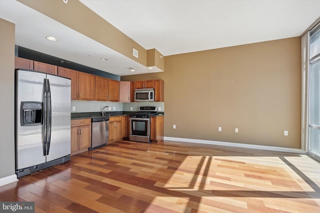 kitchen featuring baseboards, dark countertops, stainless steel appliances, light wood-style floors, and a sink