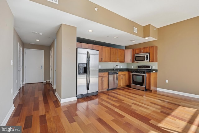 kitchen with appliances with stainless steel finishes, dark countertops, a sink, and light wood-style flooring