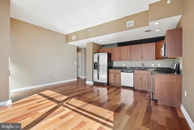 kitchen featuring visible vents, dark countertops, wood finished floors, stainless steel appliances, and a sink