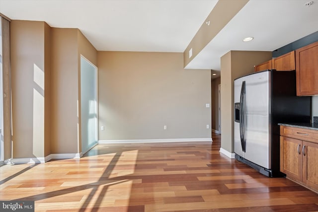 kitchen featuring brown cabinetry, light wood-type flooring, stainless steel fridge, and baseboards