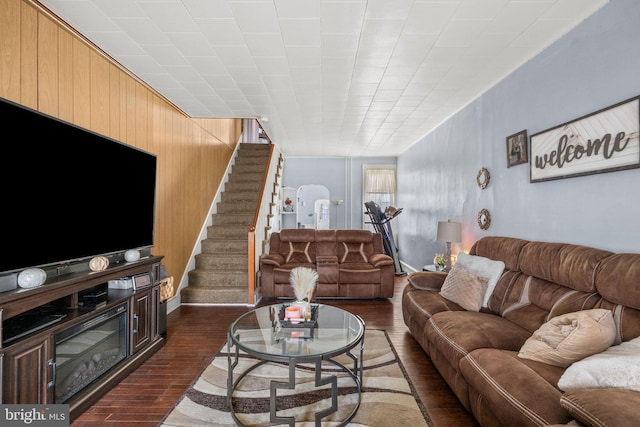 living room with dark wood-style floors, stairway, and wooden walls