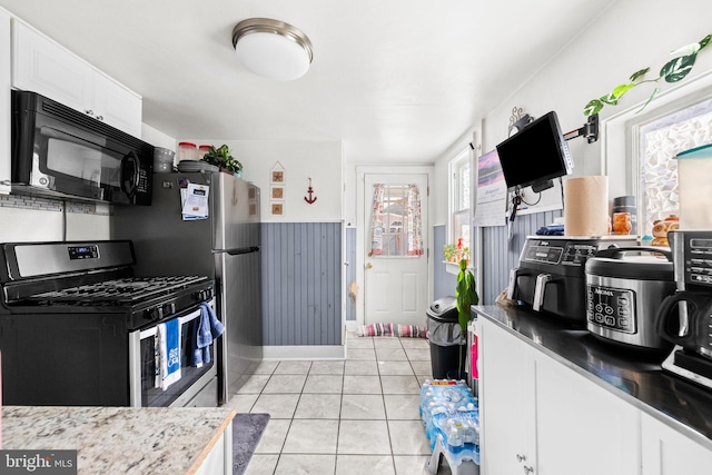 kitchen with gas stove, light tile patterned flooring, wainscoting, white cabinetry, and black microwave