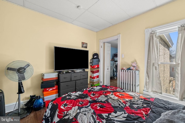 bedroom featuring radiator heating unit, a drop ceiling, and wood finished floors