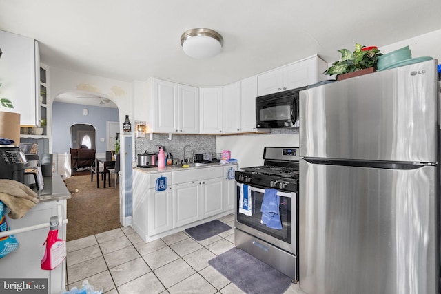 kitchen with white cabinets, arched walkways, stainless steel appliances, and a sink