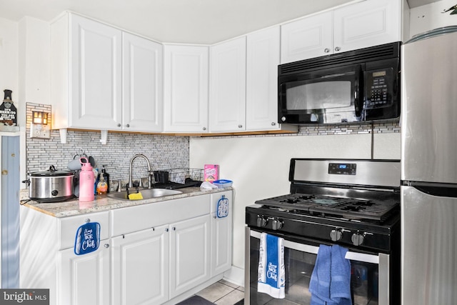 kitchen featuring light tile patterned floors, stainless steel appliances, a sink, white cabinets, and backsplash