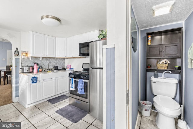 kitchen featuring white cabinets, appliances with stainless steel finishes, arched walkways, and light countertops