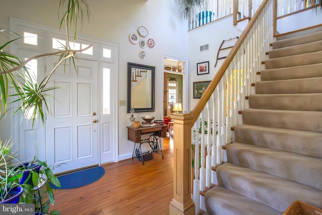 foyer with stairway, a high ceiling, visible vents, and wood finished floors