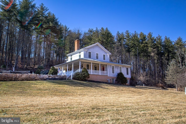 view of front facade featuring a wooded view, a porch, a chimney, and a front lawn