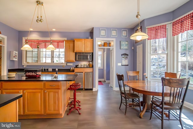 kitchen featuring stainless steel microwave, dark countertops, decorative light fixtures, and a healthy amount of sunlight