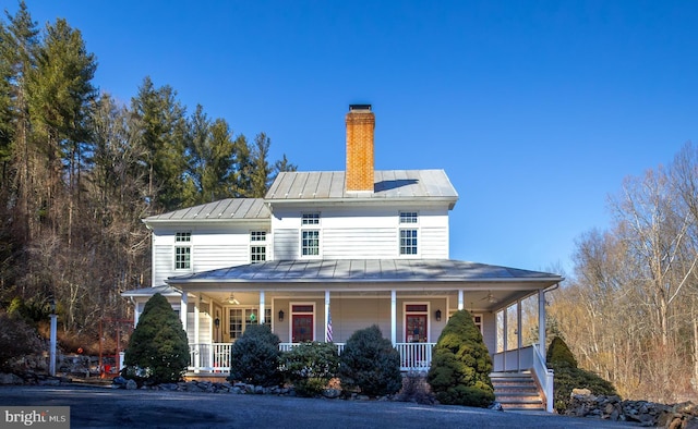 farmhouse inspired home featuring a standing seam roof, metal roof, a chimney, and covered porch